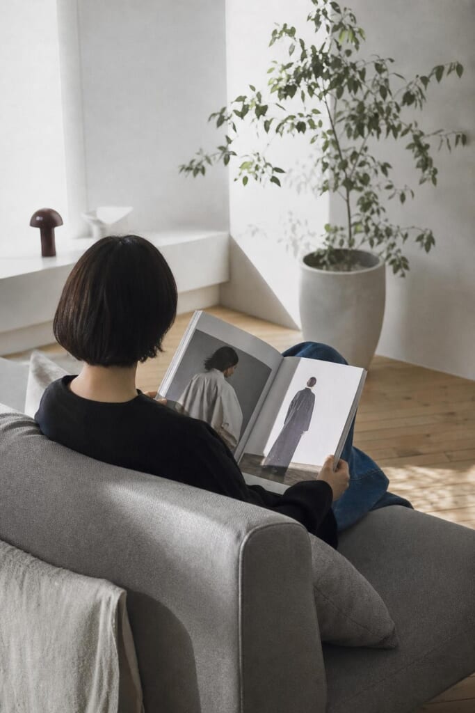 明るい部屋のソファで、大きな雑誌を読む人の後ろ姿