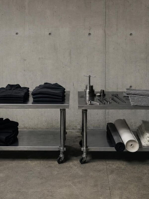コンクリートの広間に並ぶ、黒い服の作業台と、金属の工具やフェルトの作業台