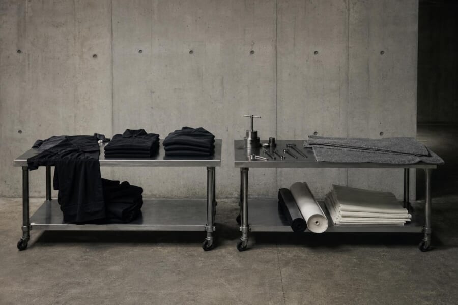 コンクリートの広間に並ぶ、黒い服の作業台と、金属の工具やフェルトの作業台